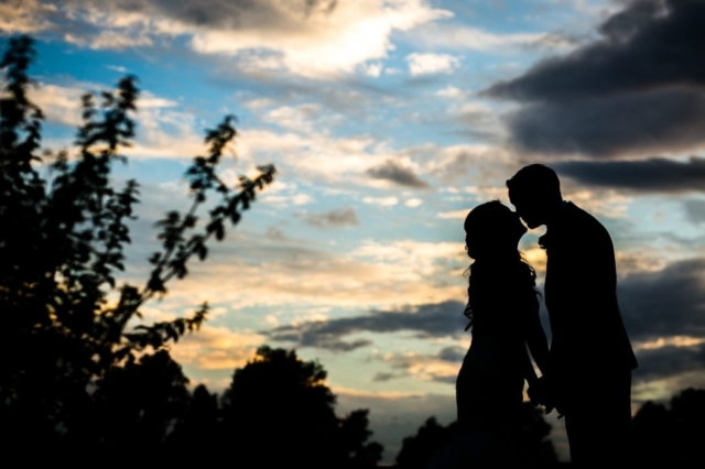 Bride and Groom kiss by sunset silhouette