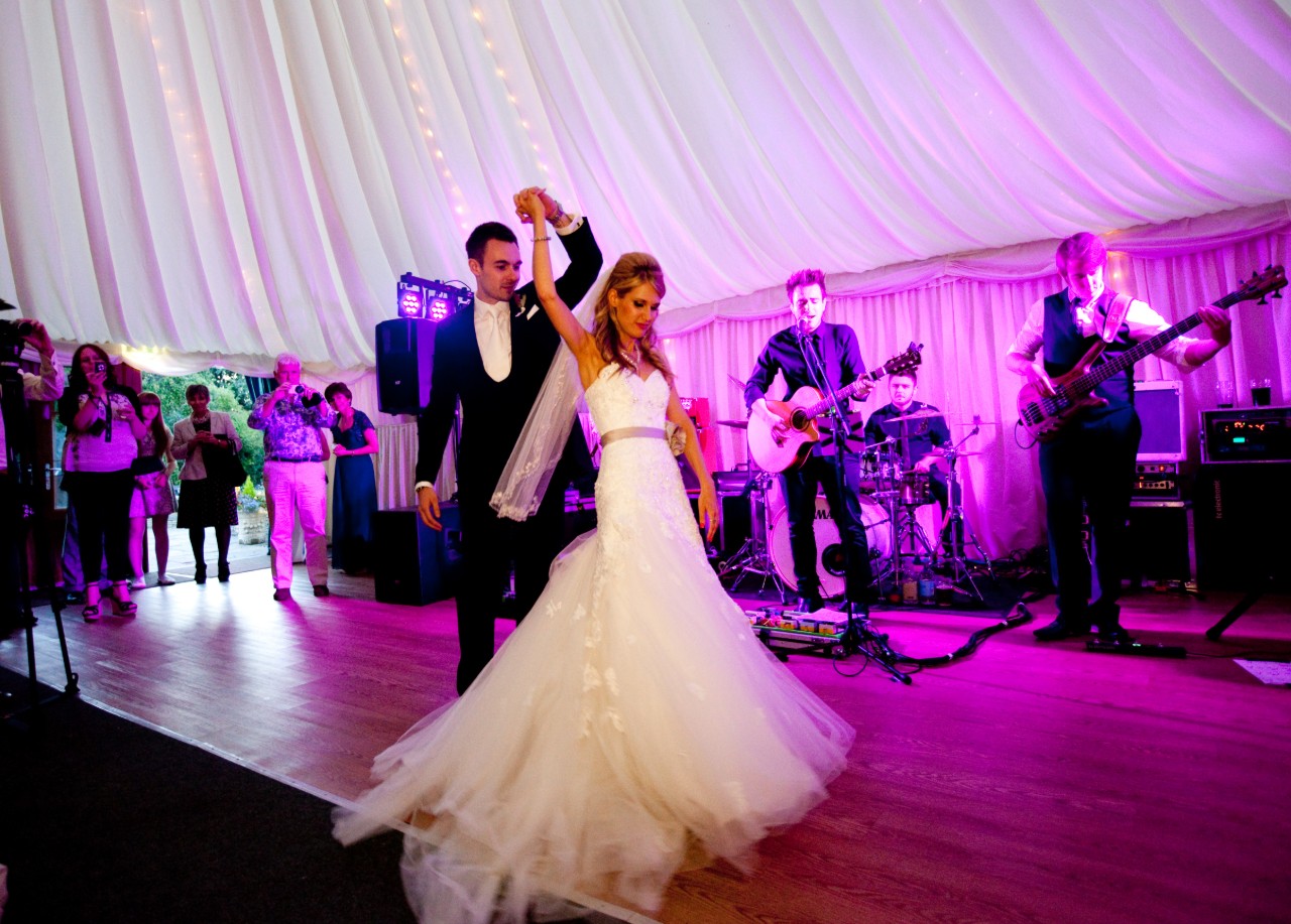 Bride and groom dancing infront of live band with pink lighting