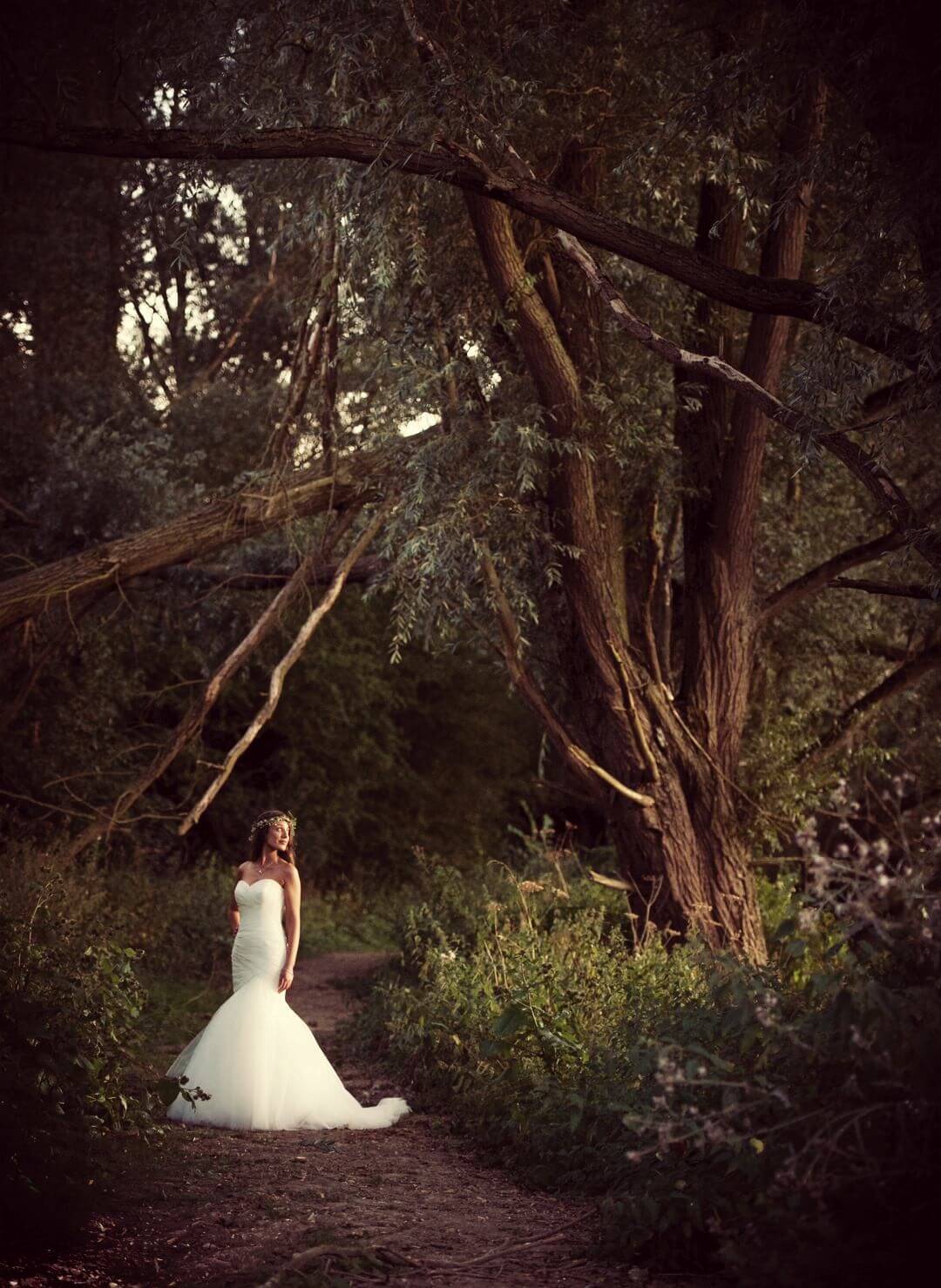 Bride posing in dark forest path looking at tree at wedding venue essex