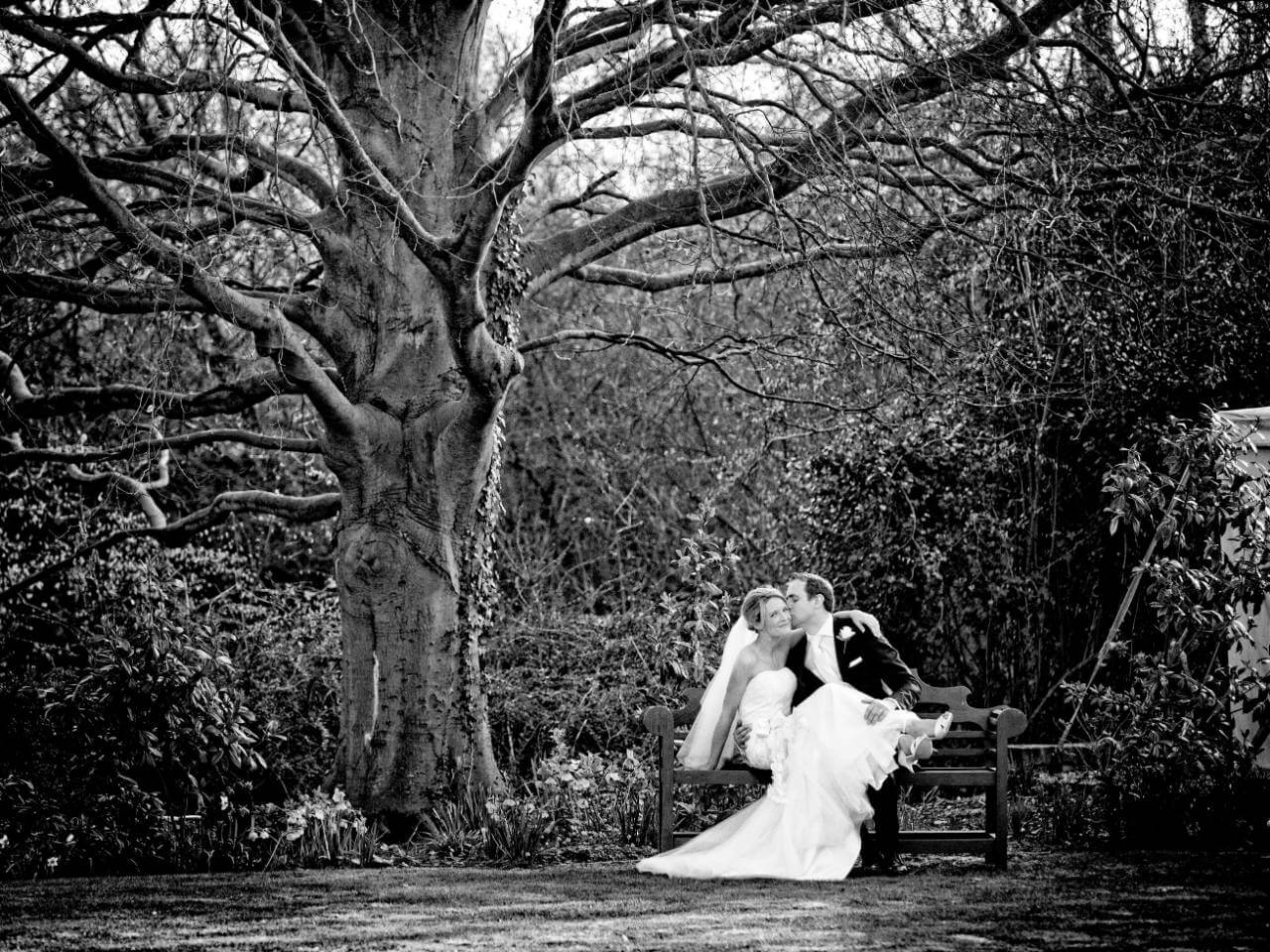 Bride and groom on bench under tree at wedding venue essex